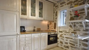 A kitchen with white cabinets, a stone wall, a window, and a shelf with flowers. - Villa Princess 6 private with Pool Panormos Beach (Mykonos)