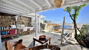 A stone-walled room with a wooden bench, a table with a bowl of fruit, and a view of the sea. - Villa Princess 6 private with Pool Panormos Beach (Mykonos)