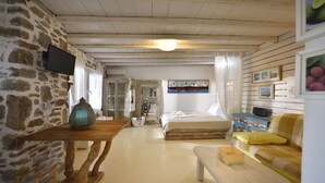 A cozy room with a stone wall, a wooden table with a vase, a bed with a canopy, and a sofa with cushions. - Villa Princess 6 private with Pool Panormos Beach (Mykonos)