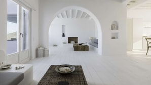 A spacious, white-themed living area with a fireplace, seating, and a view through an archway. - Villa Conza 5 bed in Mykonos (Mykonos)
