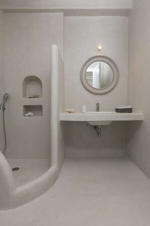 Un baño con ducha de arco, un lavabo con espejo y dos estantes con artículos de aseo.