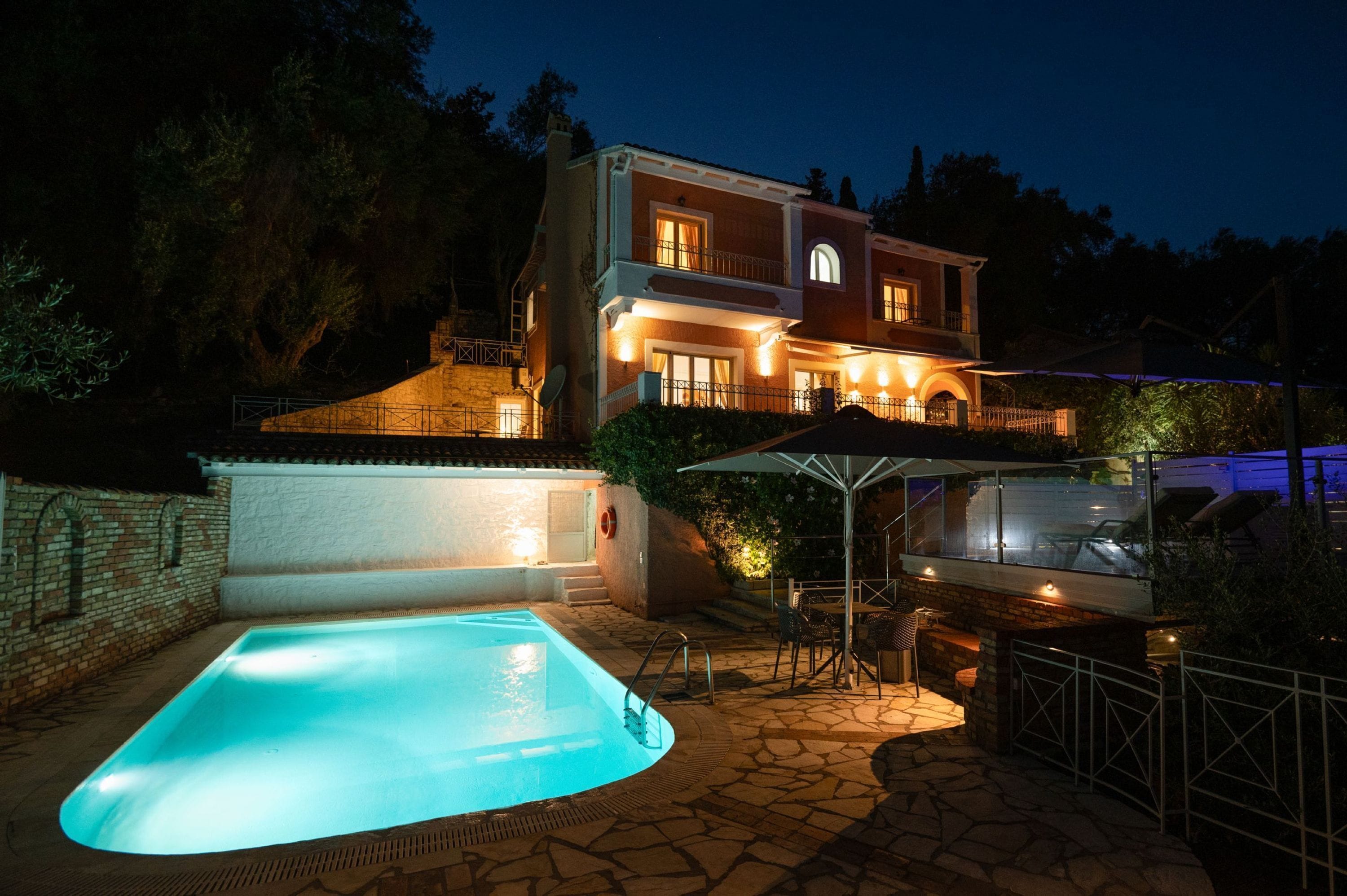 Una casa de dos pisos con piscina, mobiliario exterior y un espacio cubierto.