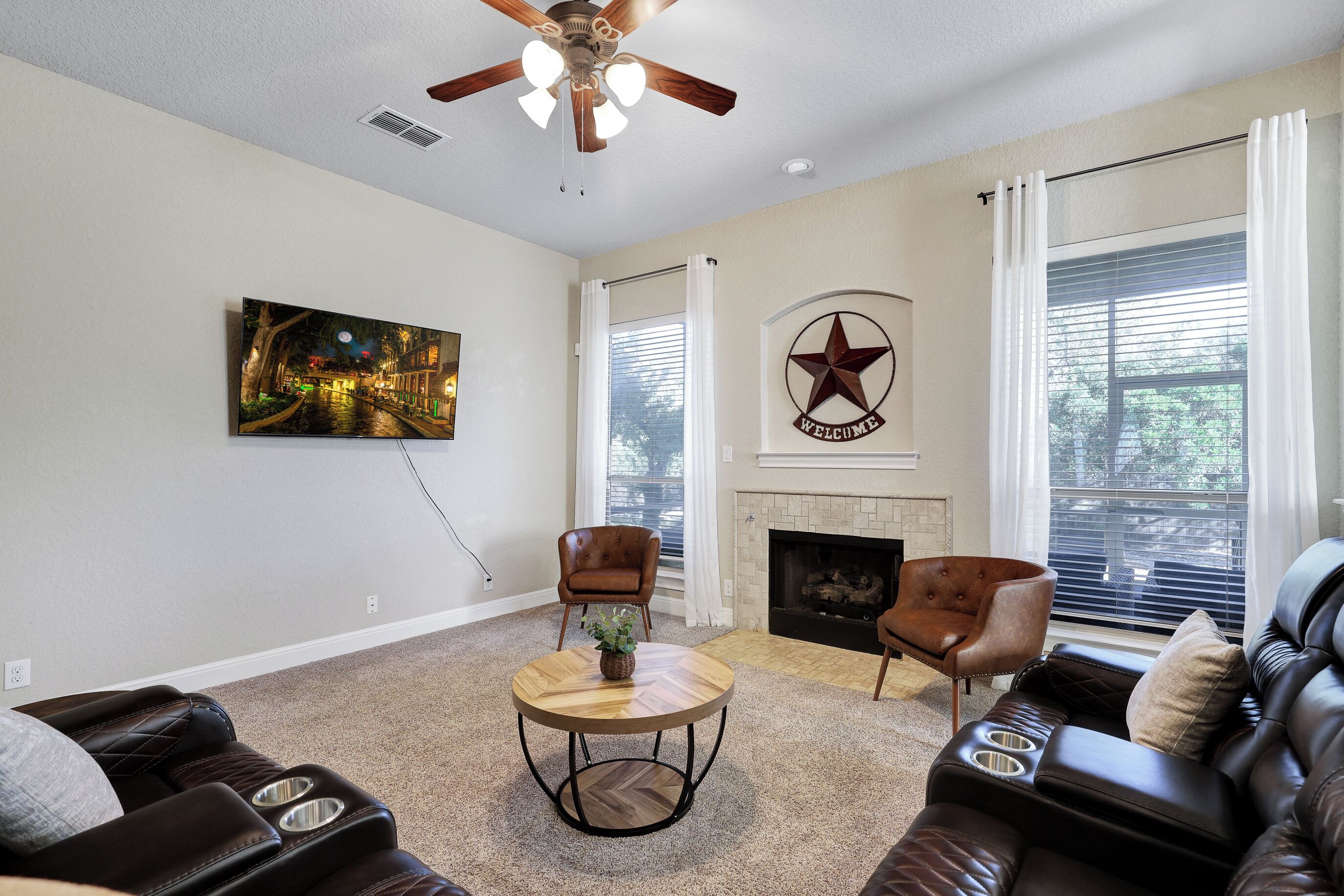 A living room with a fireplace, a ceiling fan, a round coffee table, and two leather sofas.