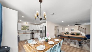 A modern kitchen with white cabinets, a dining area with a wooden table set for four, and a staircase leading to a living area.