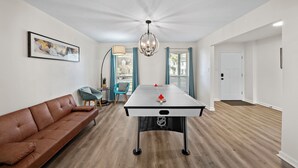 A modern living room with a brown sofa, a table football, a chandelier, and a door.