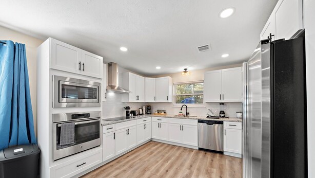A modern kitchen with white cabinets, stainless steel appliances, and a wooden floor.