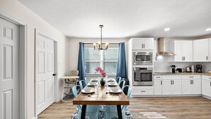 A modern kitchen with white cabinets, a dining table set for four, and a chandelier.