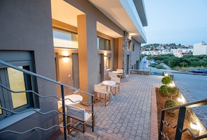 Un'area salotto esterna con tavoli e sedie, un muro in pietra e vista su una zona residenziale.