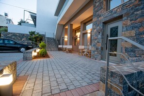 A hotel entrance with a paved walkway, outdoor seating, and a staircase leading to the entrance.