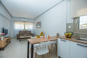 A modern living space with a dining area, a sofa, a television, and a kitchen counter with a fruit bowl.