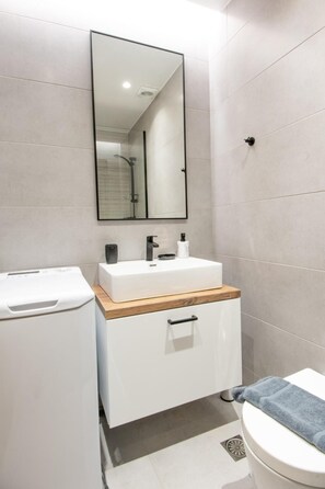 A modern bathroom with a white sink, mirror, and toilet.