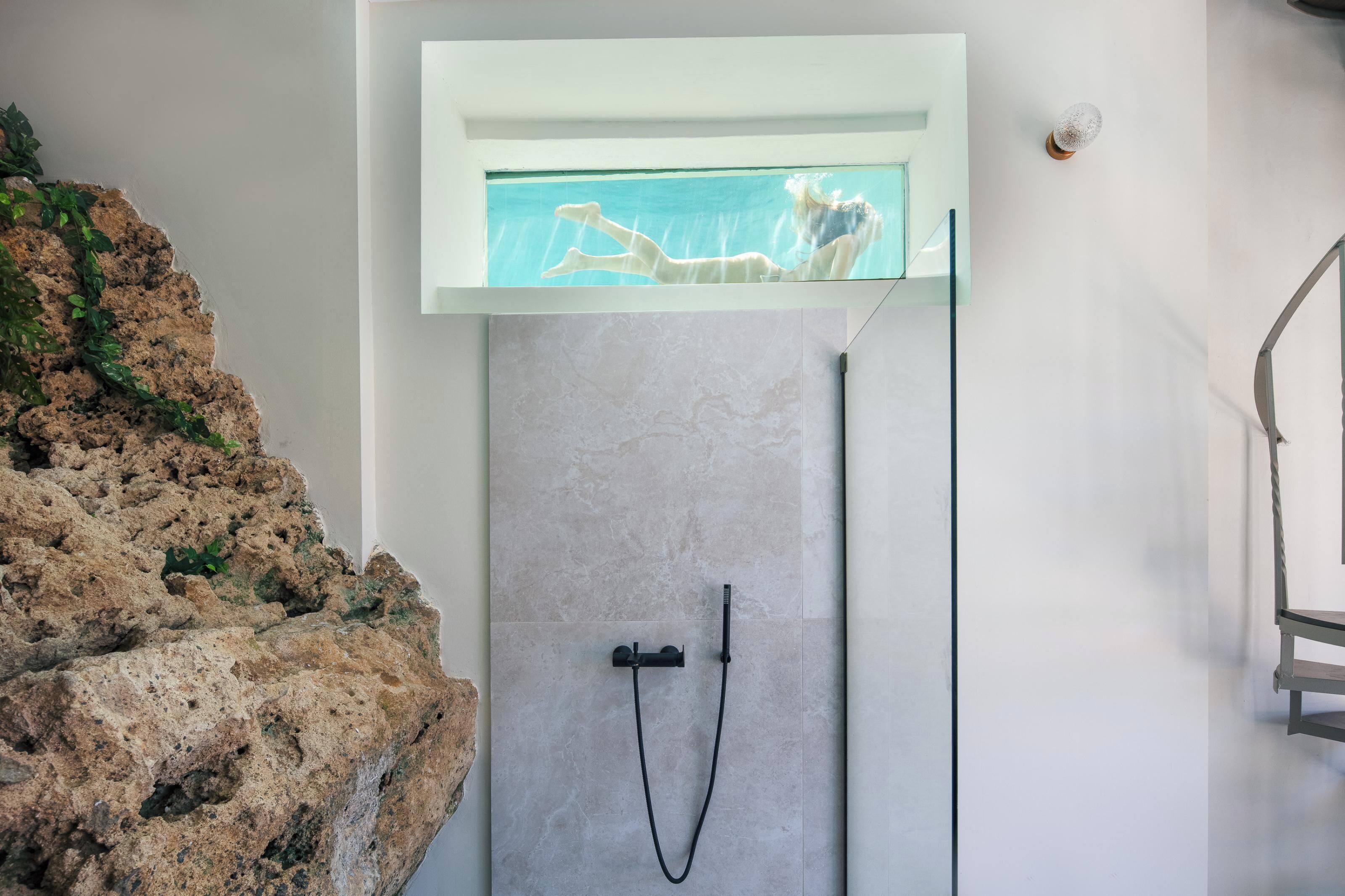 Un baño moderno con pared de piedra, cabina de ducha de vidrio y elemento decorativo de roca integrado.