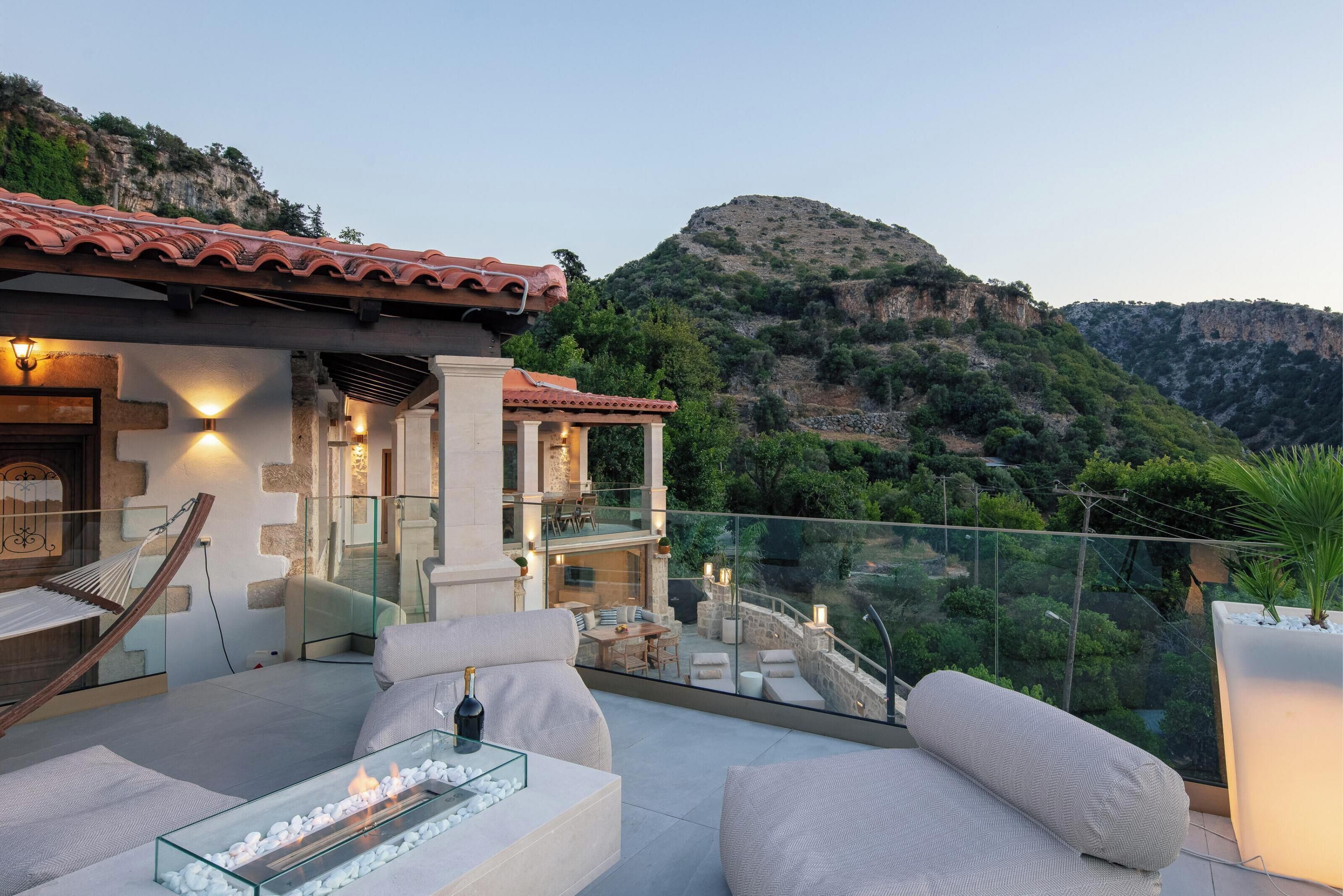 A modern outdoor seating area with a glass-top table, cushioned chairs, and a fire feature.