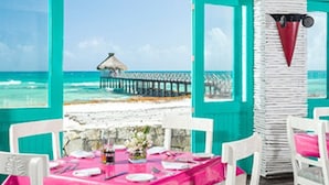 Un coin repas avec une table dressée pour deux personnes, donnant sur une plage avec une jetée.