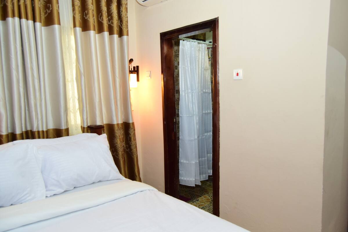 Une chambre d’hôtel avec un lit, des rideaux et une porte donnant sur une salle de bain.