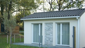 A modern building with a tiled roof, large glass windows, and a stone accent wall. - Romantic room in nature (Lunas)