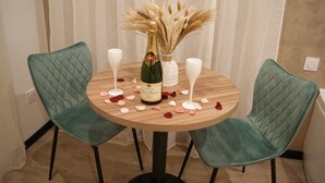 A round wooden table with two teal chairs, a bottle of champagne, and a vase with dried pampas grass. - Romantic room in nature (Lunas)