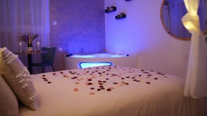 A bedroom with a bed, a chair, a small table with a bottle, and a bathtub. - Romantic room in nature (Lunas)