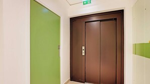 A hallway with a green door and a brown elevator door. - Studio Sleek & Refined - Levallois-Perret (Levallois-Perret)