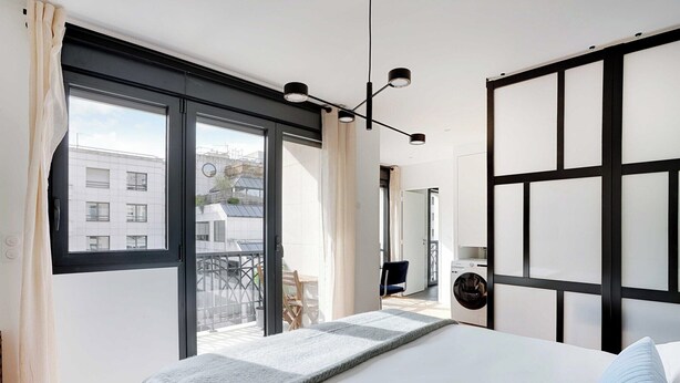 A modern bedroom with a large bed, a view of the balcony, and a black-framed headboard. - Studio Sleek & Refined - Levallois-Perret (Levallois-Perret)