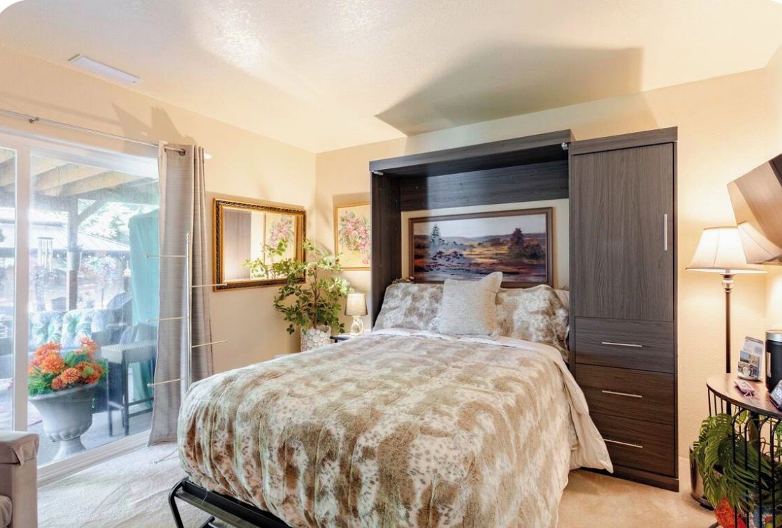 Un dormitorio con una cama grande, una mesita de noche, una lámpara, una ventana con cortinas y vistas al exterior.