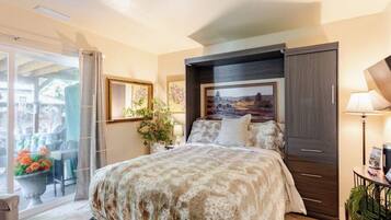 Un dormitorio con una cama grande, una mesita de noche, una lámpara, una ventana con cortinas y vistas al exterior.