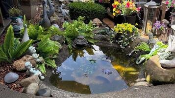 Un jardín con un estanque, diversas plantas y estatuas decorativas.