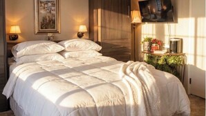 A hotel room with a large bed, two bedside tables with lamps, a television on the wall, and a window with sunlight.