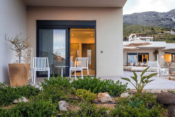 A modern building with a glass door entrance, white chairs, and a patio area with outdoor seating.