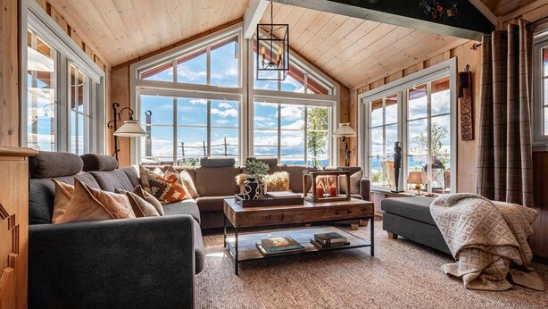 A cozy living room with a high ceiling, large windows, and a fireplace.