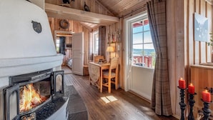 A cozy cabin interior with a fireplace, wooden walls, a dining area, and a view through a large window.