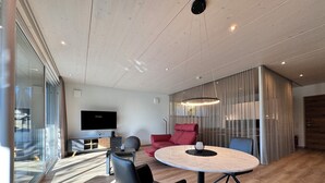 Un salon moderne avec une table à manger ronde, des chaises noires, un canapé rouge et un téléviseur à écran plat fixé au mur.