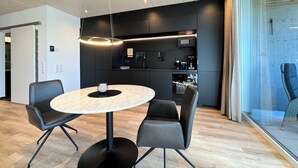 Une cuisine moderne dotée d’appareils électroménagers intégrés, une table de salle à manger ronde avec des chaises, et une cloison en verre.