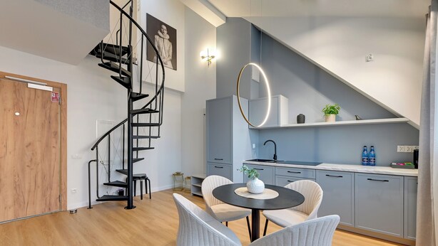 A modern kitchen with grey cabinets, a black spiral staircase, and a round mirror.