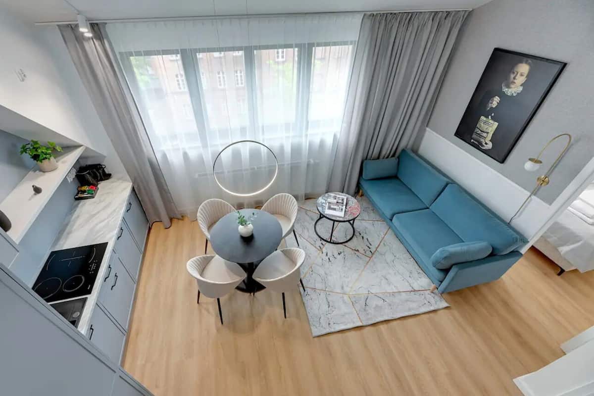 A compact living space with a kitchenette, a round dining table with chairs, a blue sofa, a small coffee table, and a large window with curtains.
