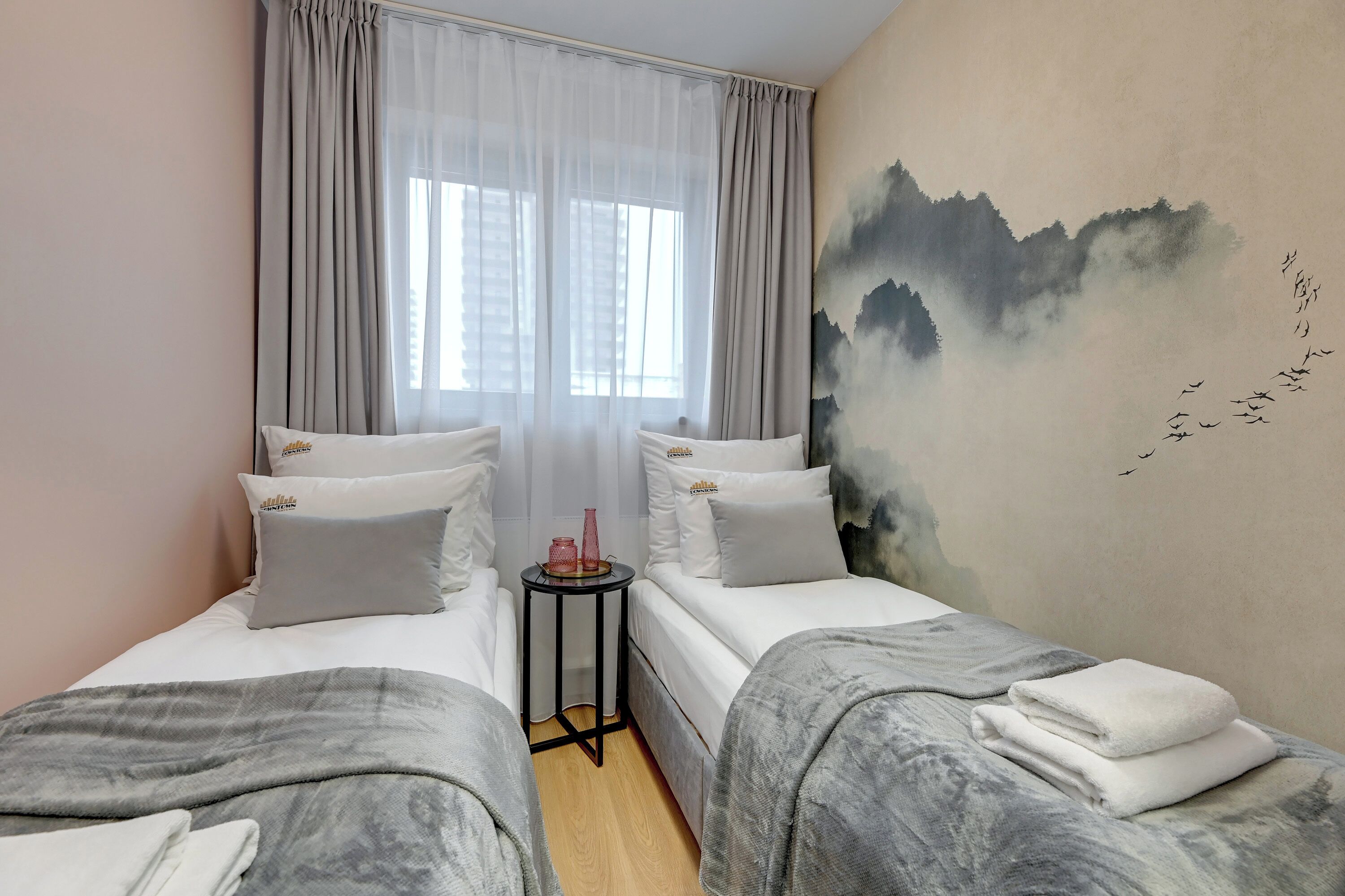 Una habitación de hotel con dos camas, una mesita y un mural en la pared.