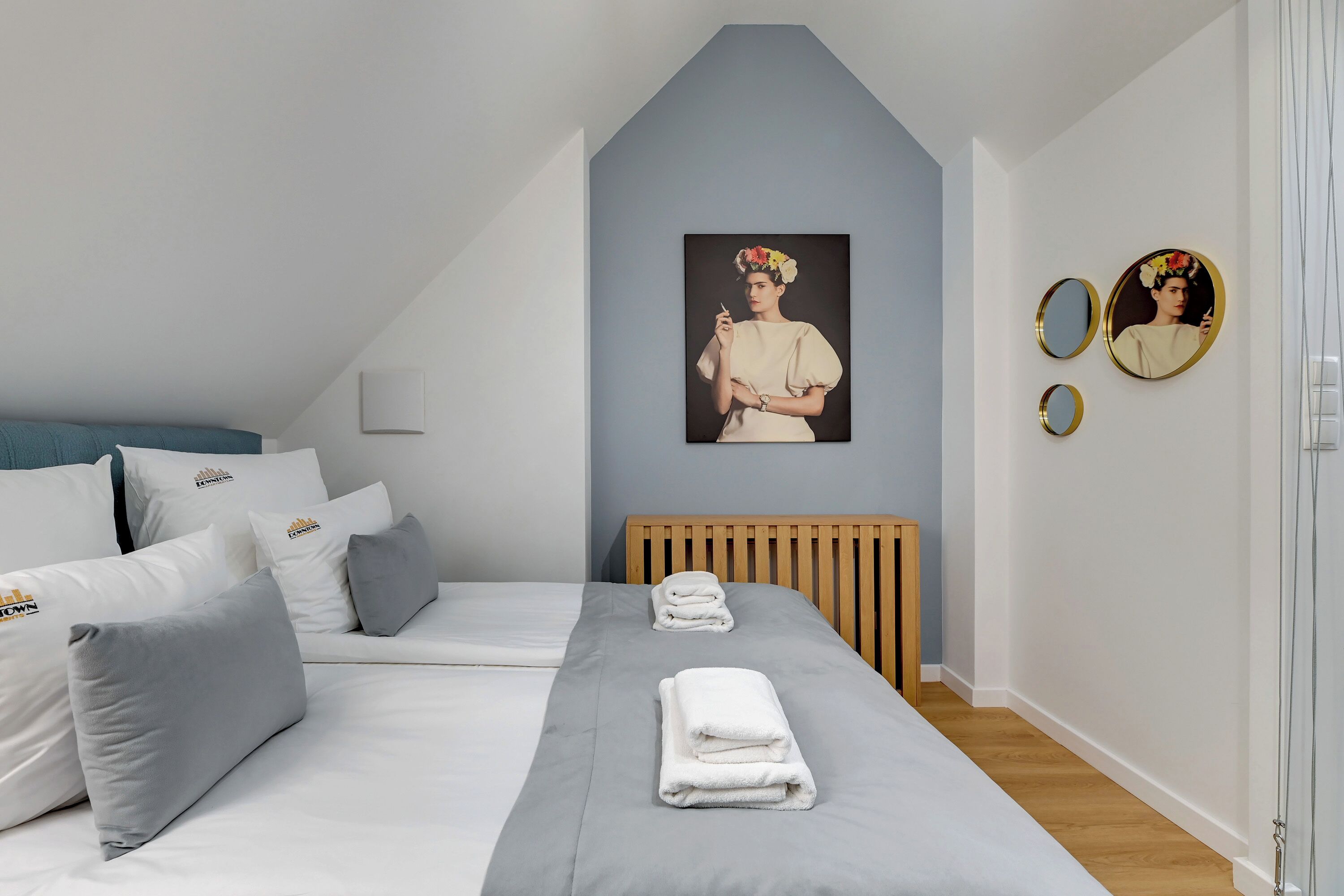 Ein modernes Schlafzimmer mit schrägen Wänden, einem Bett mit grauer Bettwäsche, zwei Nachttischen, einem hölzernen Kopfteil und einem an der Wand montierten Heizkörper.