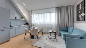 A modern living room with a blue sofa, a dining table with chairs, and a kitchen area with grey cabinets.
