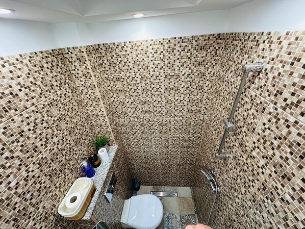 A bathroom with a mosaic tile wall, a toilet, a shower, and a sink with toiletries. - Urban Studio for a Real Ghetto Experience (Craiova)
