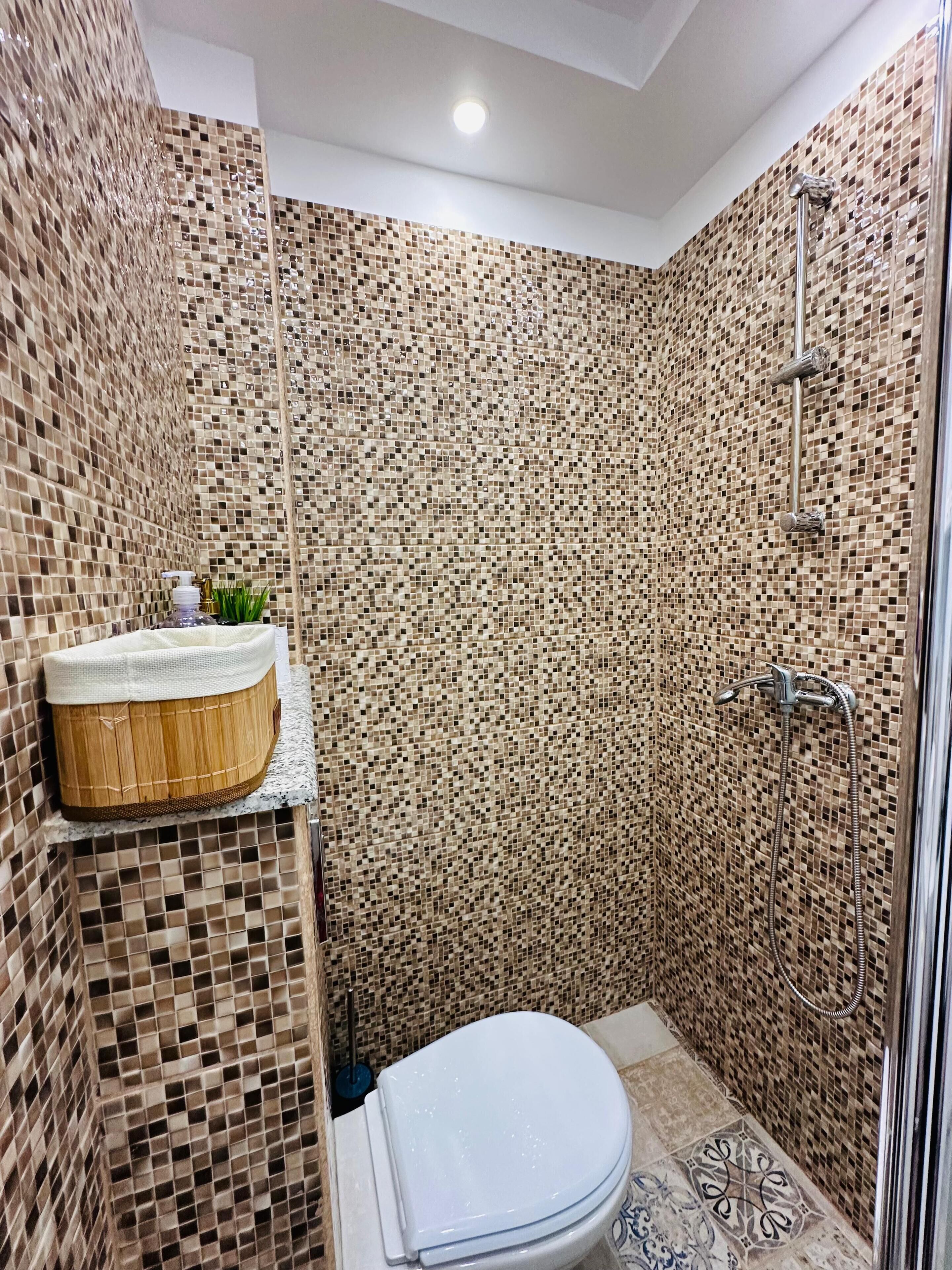 A bathroom with mosaic tile walls, a wooden vanity with a sink, and a shower area.