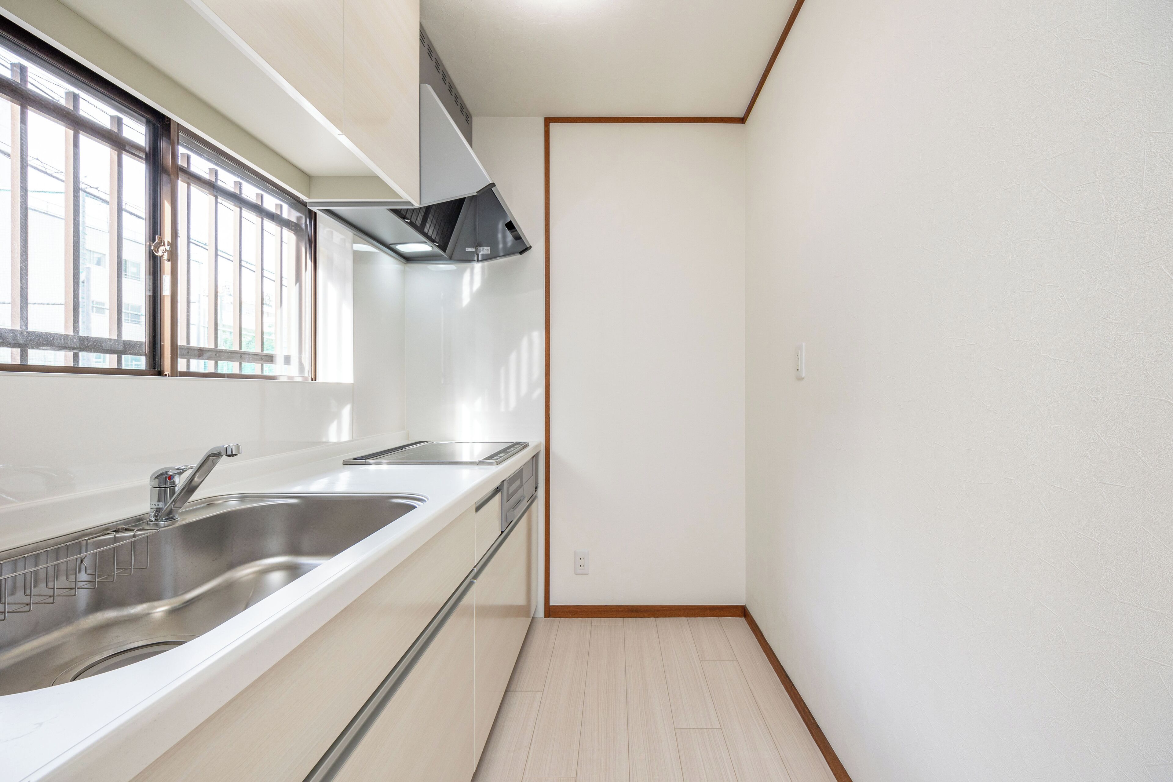 A modern kitchen with a stainless steel sink, a window with blinds, and a white countertop.