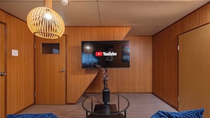 Ein modernes Zimmer mit Holzvertäfelung, einem runden Glastisch mit einer Vase und einem Flachbildfernseher, der das YouTube-Logo zeigt.