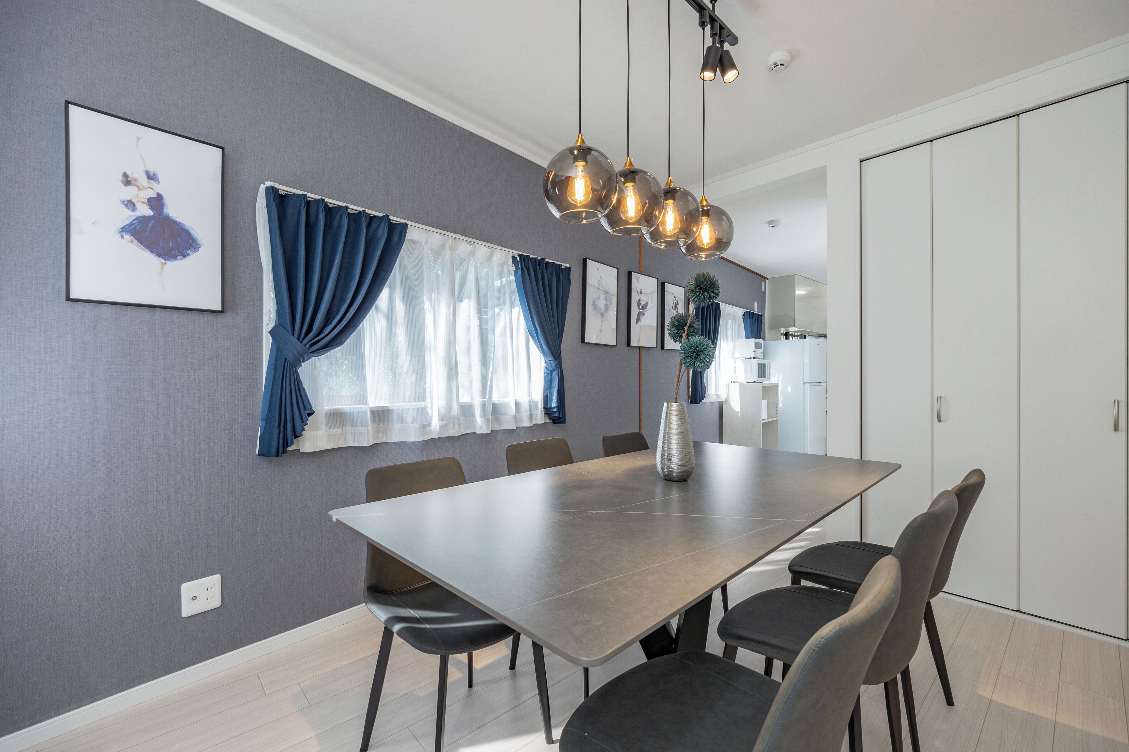 A modern dining area with a long table, chairs, and pendant lighting.
