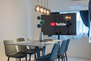A modern dining area with a glass table, black and blue chairs, and a decorative vase. - Aquamarine House (Osaka)