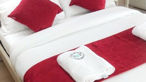 A neatly made double bed with white bedding and red pillows, a white towel with a logo, and a red throw blanket. - Tranquil Retreat in Gorebridge (Gorebridge)