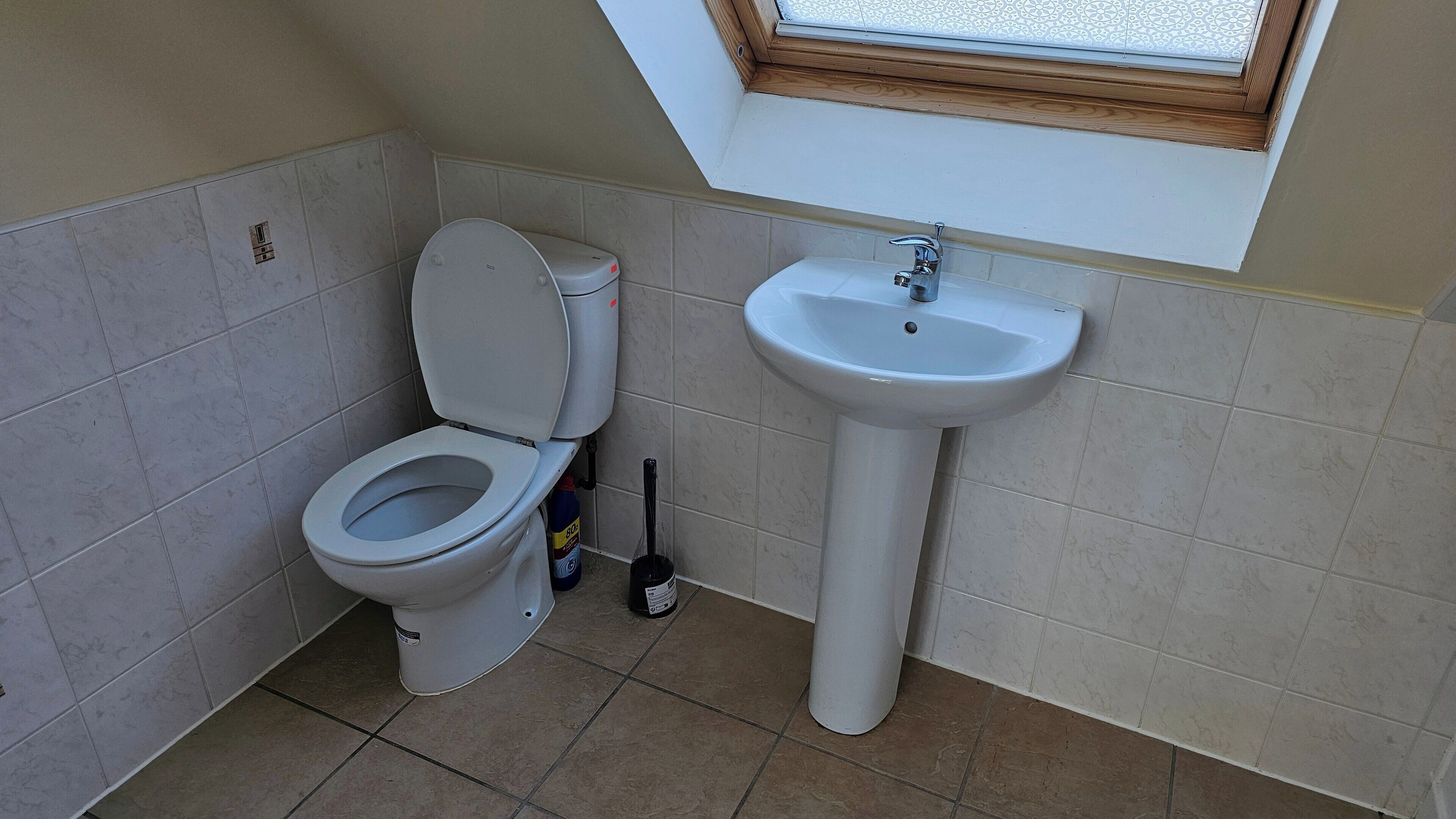 A bathroom with a toilet, a sink, and a window above the sink.