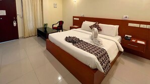 A hotel room with a bed, a desk, a chair, a ceiling fan, and a door. - Hotel Sasthapuri (Kozhikode)