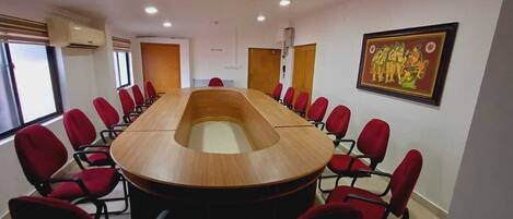 A conference room with a long table and red chairs, large windows, and a framed picture on the wall.