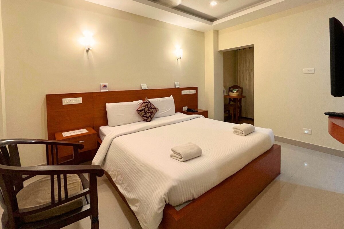 A hotel room with a large bed, a wooden headboard, bedside tables, a chair, a desk, and a ceiling fan.