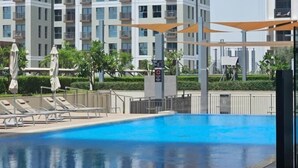 Piscina con sillas de descanso y sombrillas, rodeada por un edificio residencial alto.